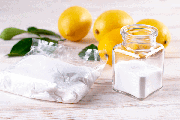 Lemons and a jar of white powder, possibly a natural cleaning agent, displayed on a wooden surface.
