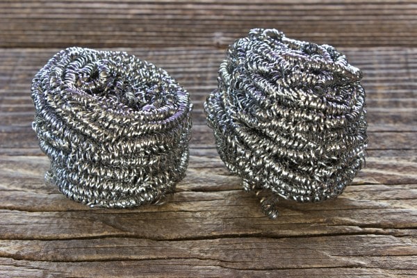 Two steel wool sponges stacked on a wooden surface.