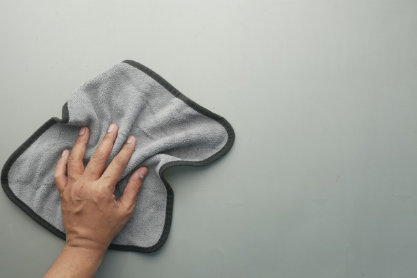 Hand wiping surface with gray microfiber cleaning cloth.
