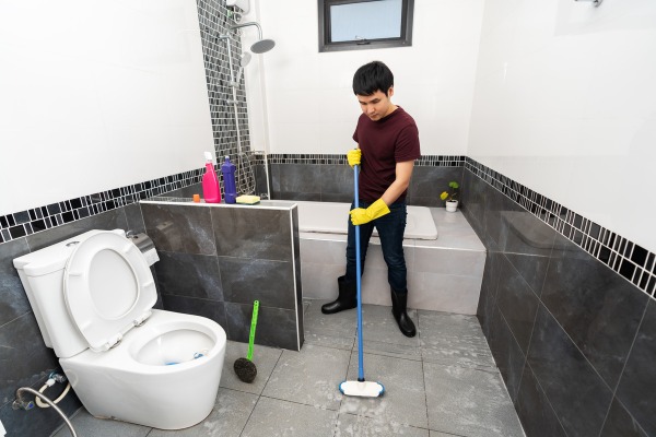 Man mopping bathroom floor with toilet and bathtub.