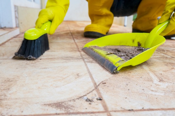 Person sweeping dirt into yellow dustpan on tiled floor.