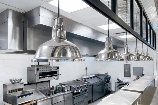 Professional commercial kitchen with stainless steel appliances and pendant lights.