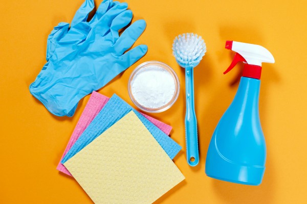 Cleaning tools with gloves, spray, brush, and sponges on orange background.
