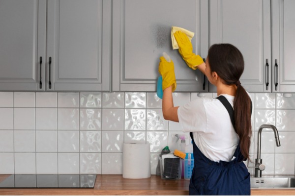 a woman in apron cleaning kitchen cabinet with cloth