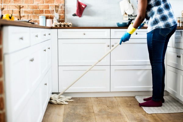 
Woman mopping kitchen floor with white cabinets.