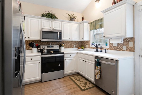White kitchen with appliances, wooden floor, and tiled backsplash.