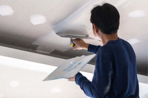 Person applying joint compound to ceiling with trowel.