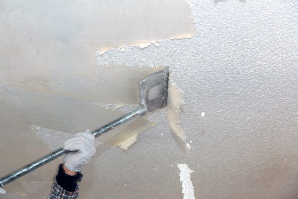 Removing textured popcorn ceiling using scraping tool.
